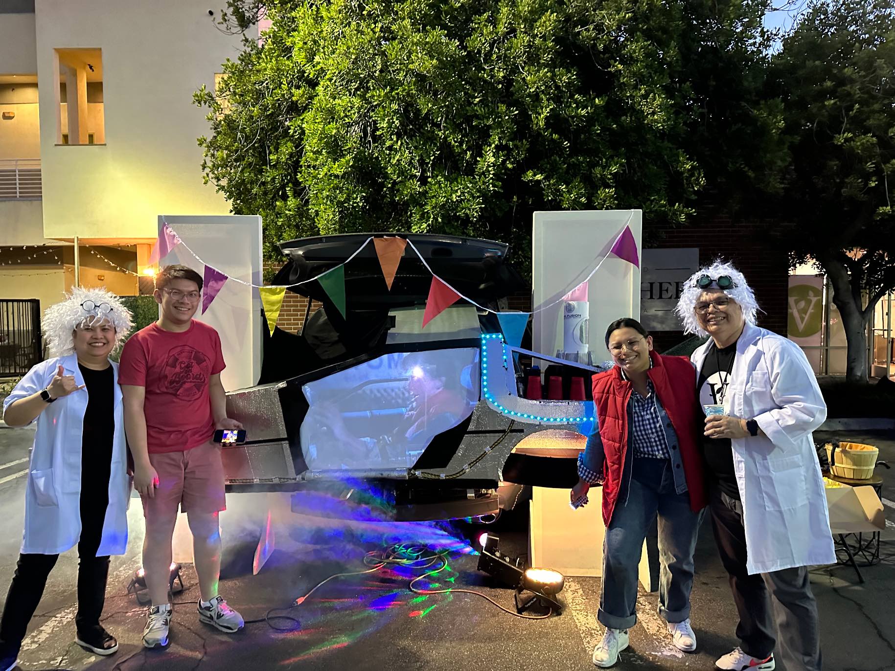 Four volunteers stand in costumes near their car that is themed from Back to the Future.