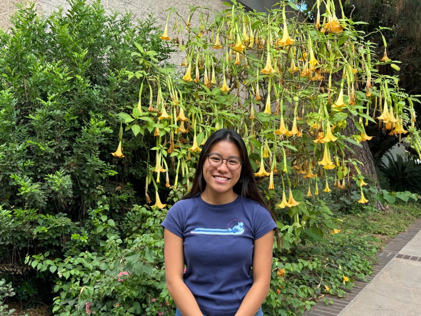 Abi smiles outside on east campus near trees and flowers