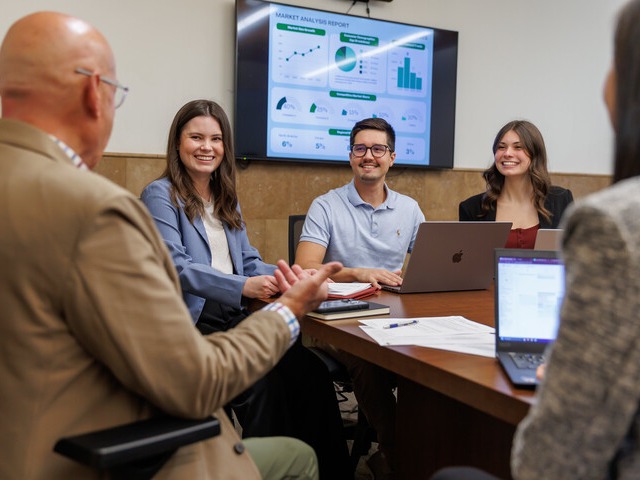 Three students sit at a conference table with laptops 