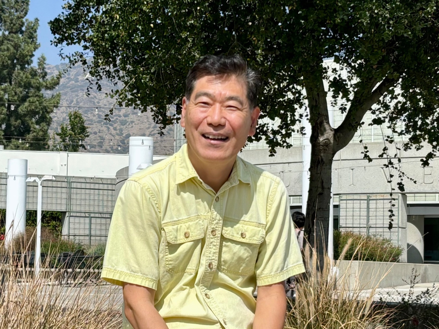 heekap smiles outside west campus near trees and the library