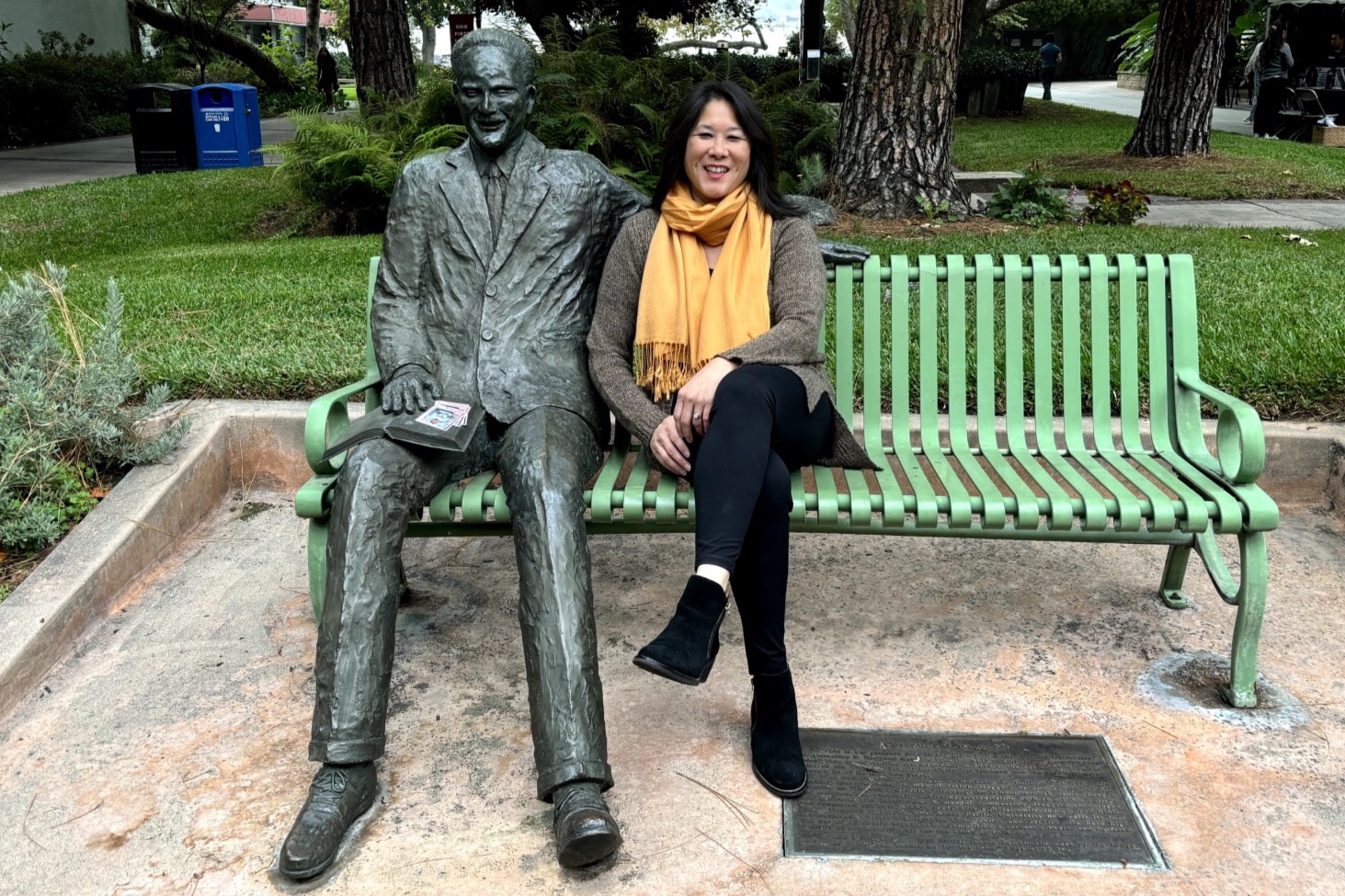 Kim sits on a bench on cougar walk with a statue of one of apu's former presidents