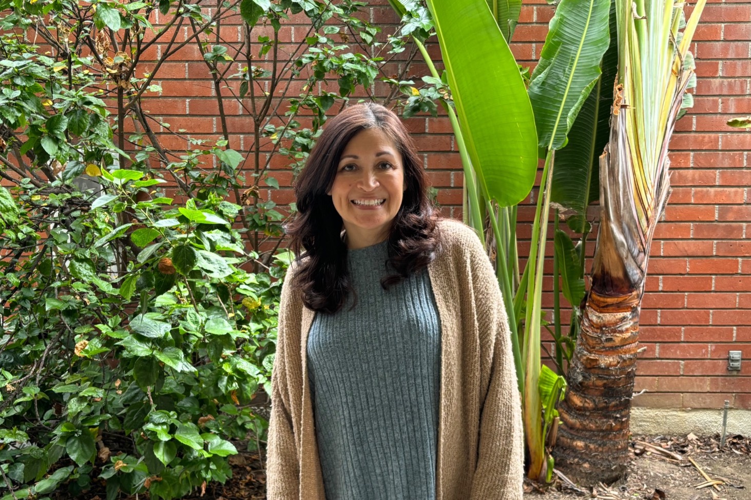 monica smiles outside her office near plants and a brick wall