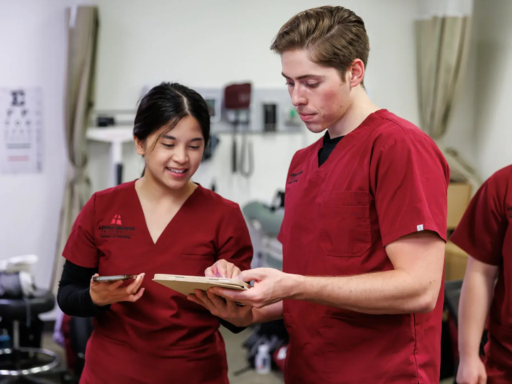 Two students in scrubs looking at a chart