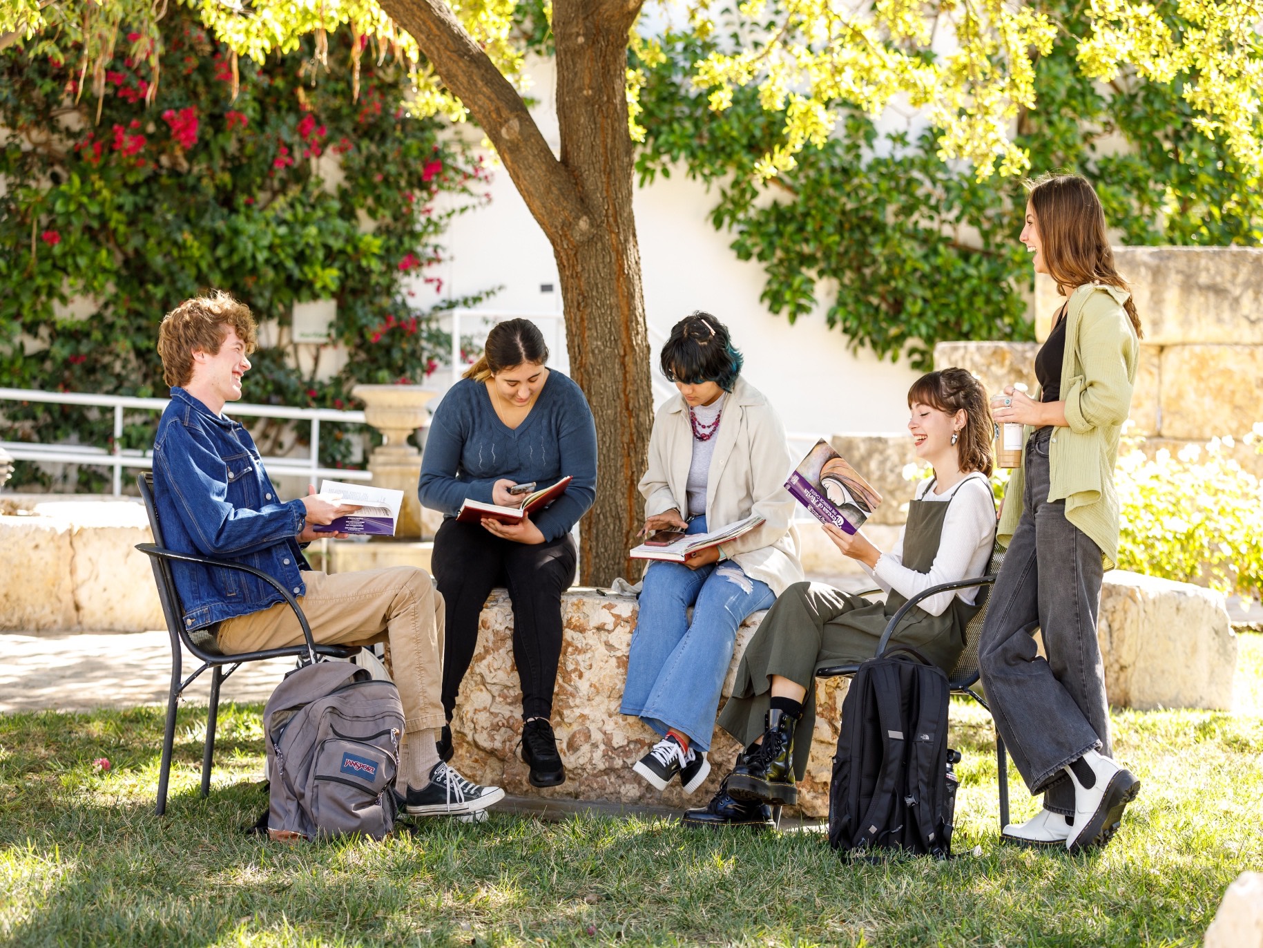 five students sitting in the prayer garden laughing while doing homework together