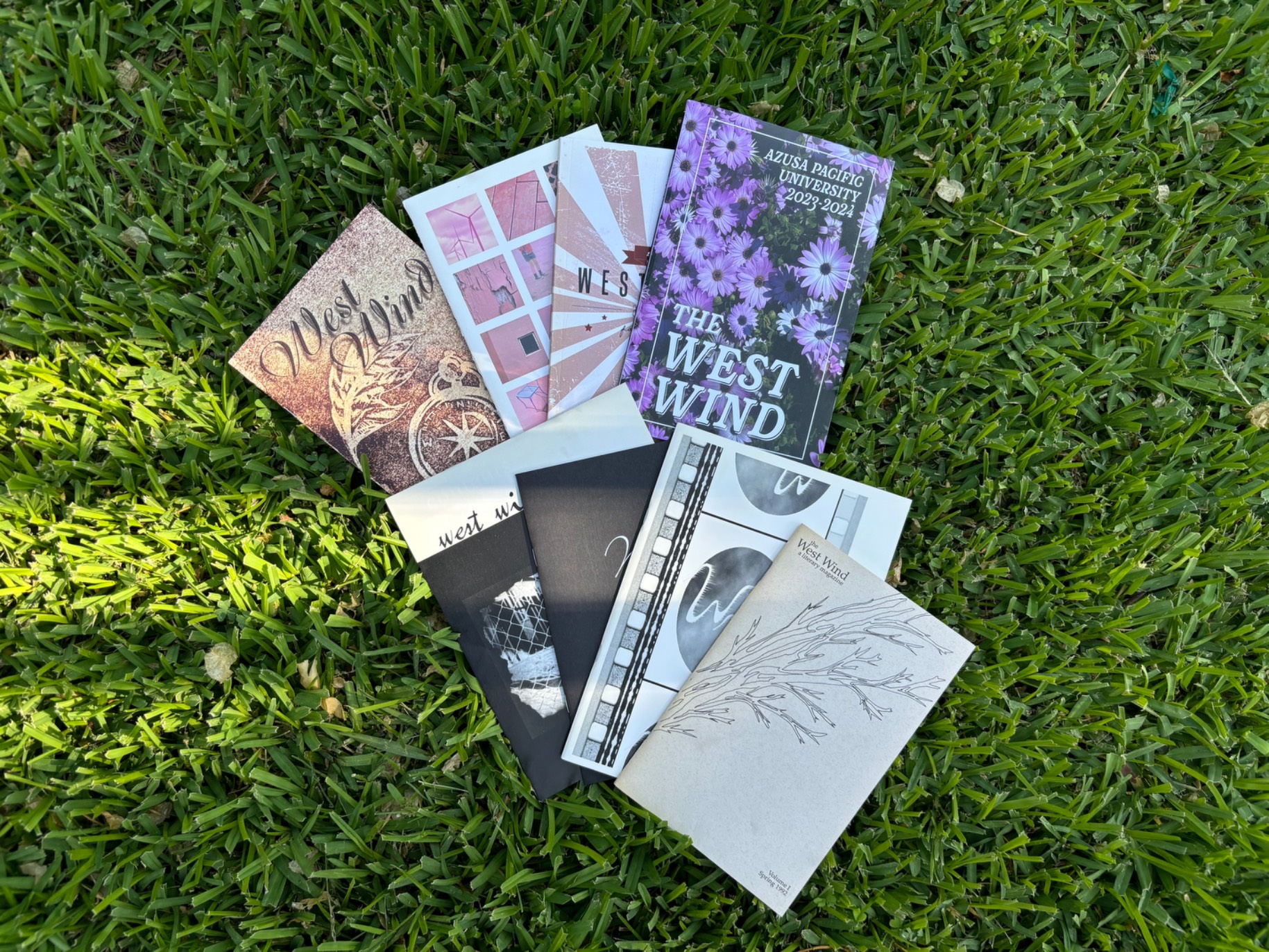 several editions of the west wind from 1992-2024 displayed on grass