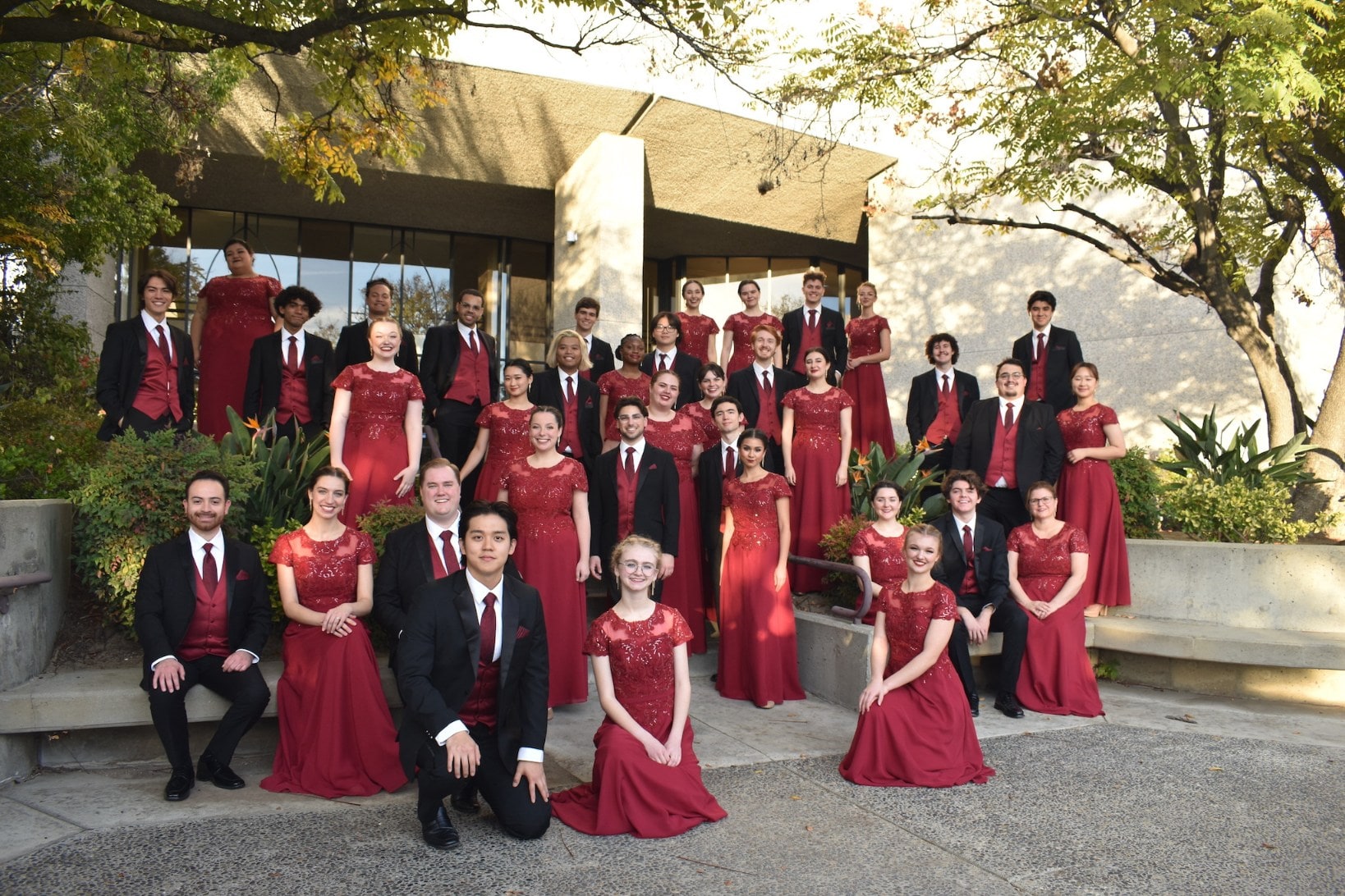 Image of the chamber singers in front of the darling library at APU wearing black suits and blue dresses.