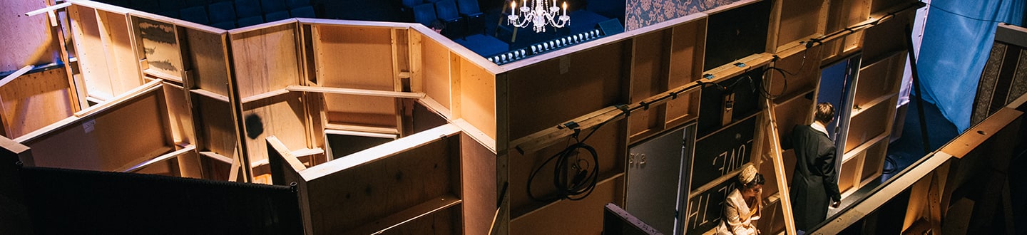 Unfinished theater stage with wooden scaffolding contrasted against an ornate chandelier backdrop