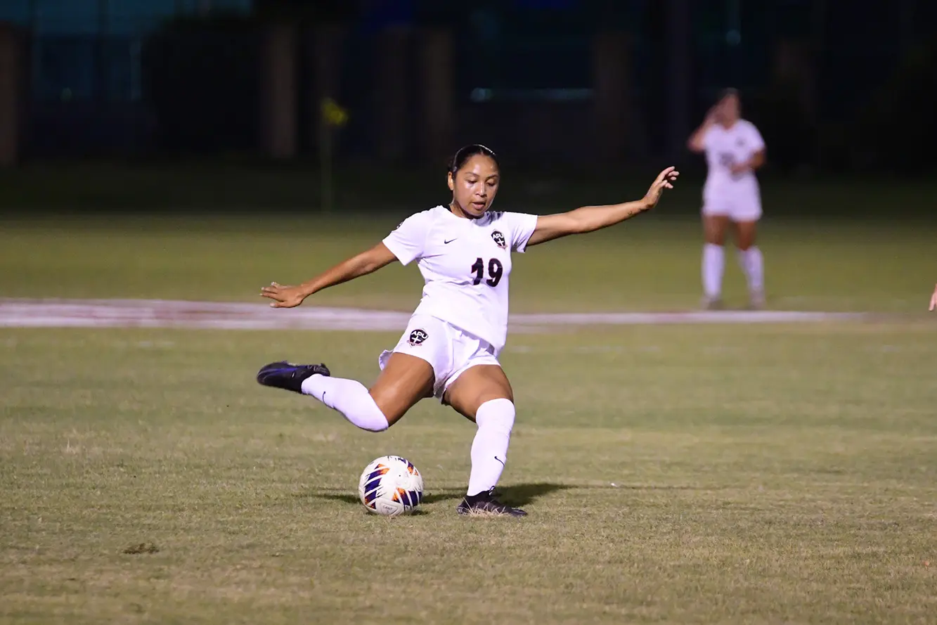 APU female soccer player kicking a ball in night game