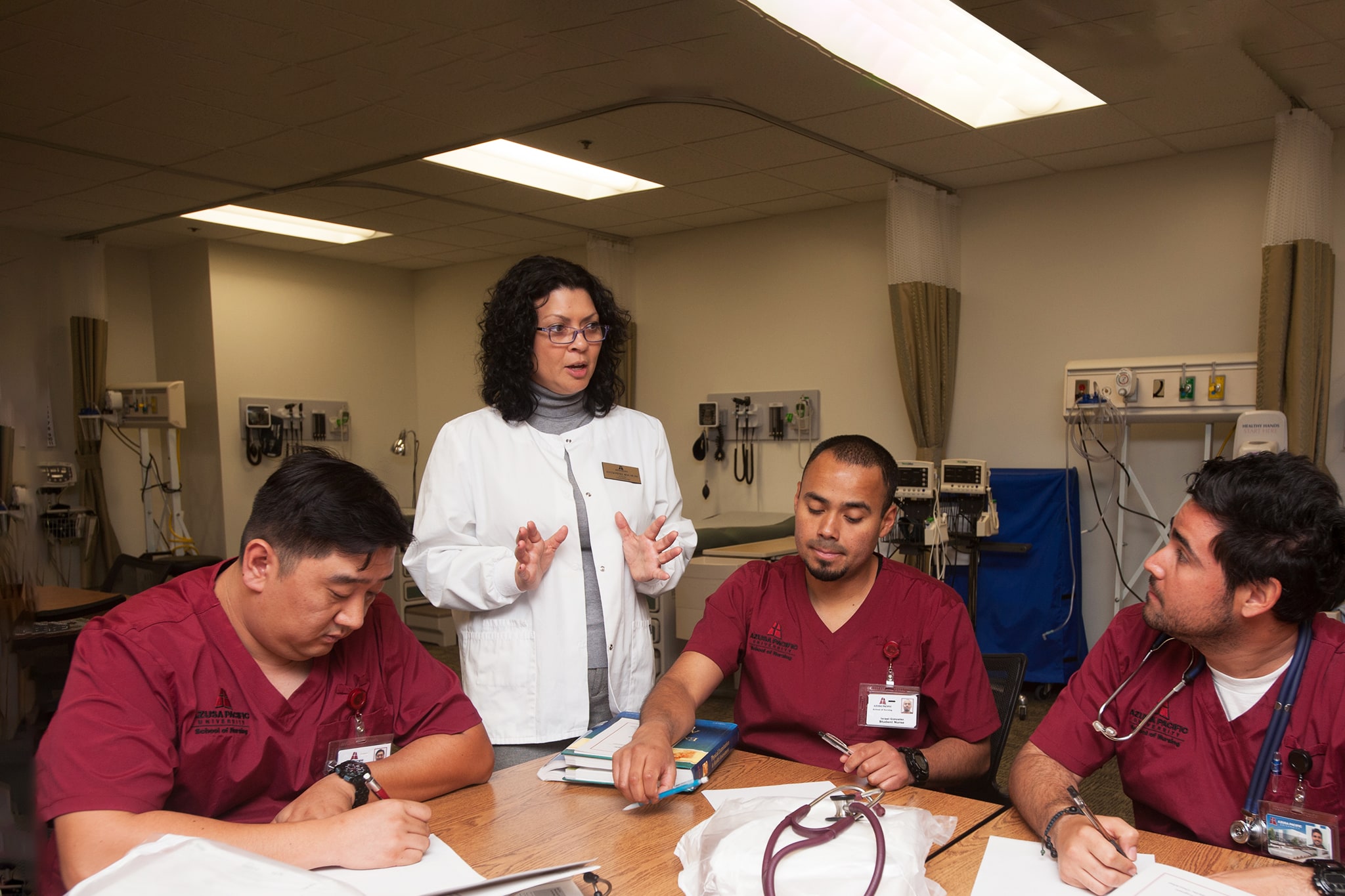 Nursing professor in white speaking to three nursing students