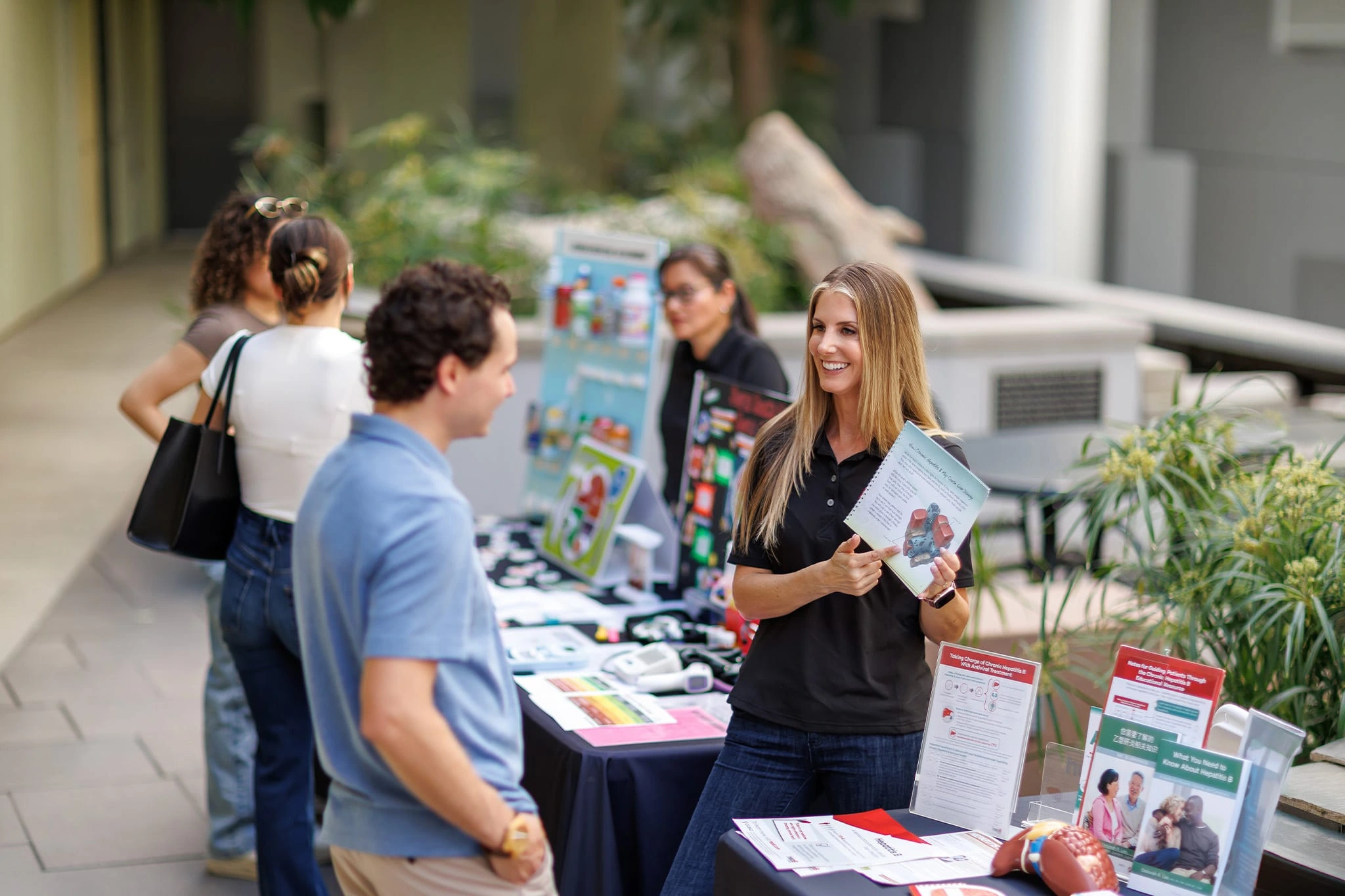 A medium shot of two people talking and smiling at each other by a stand covered with informative leaflets and pamphlets, surrounded by other stands.