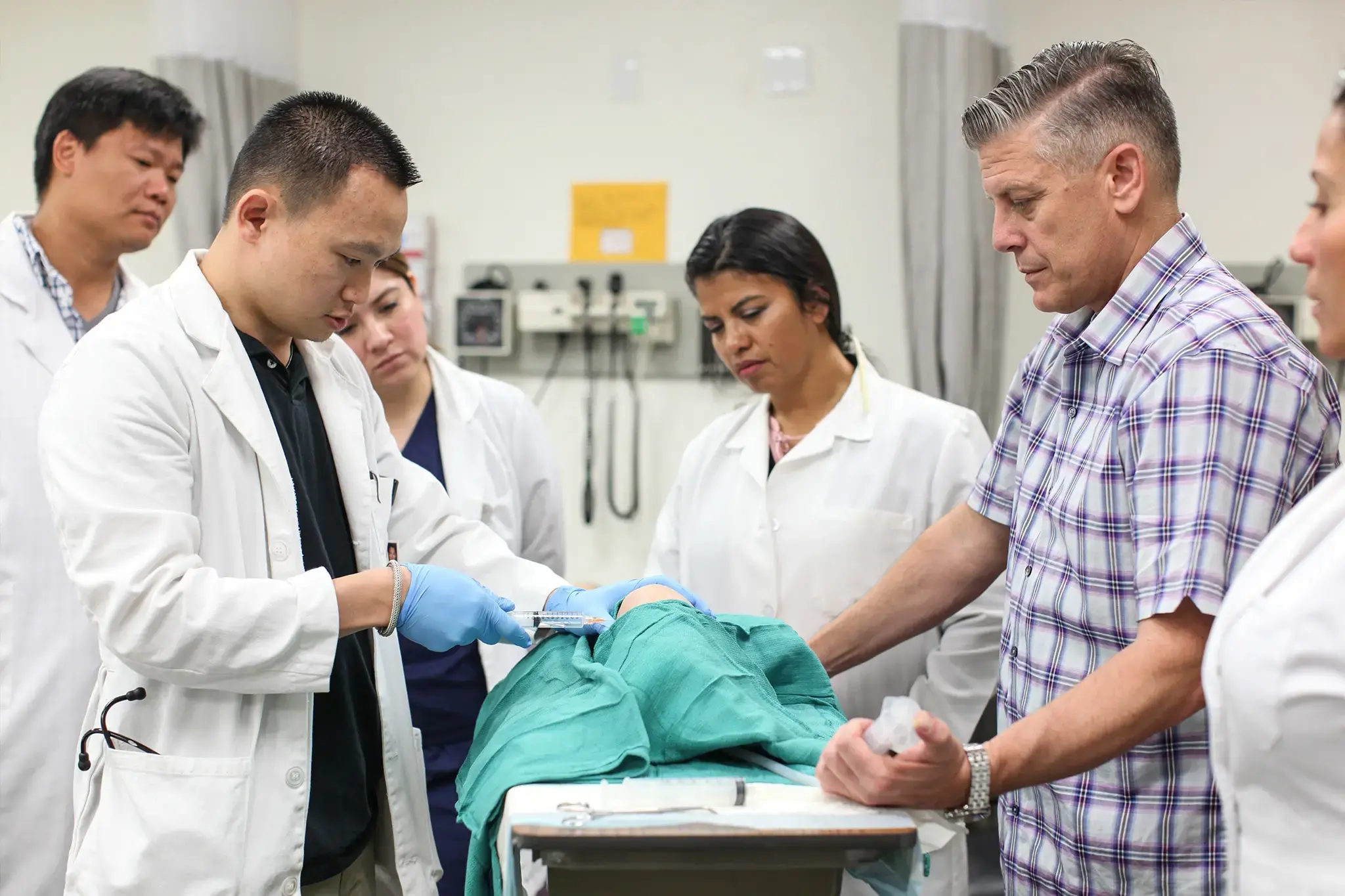 Nursing students practice a clinical procedure on a patient simulator while an instructor observes